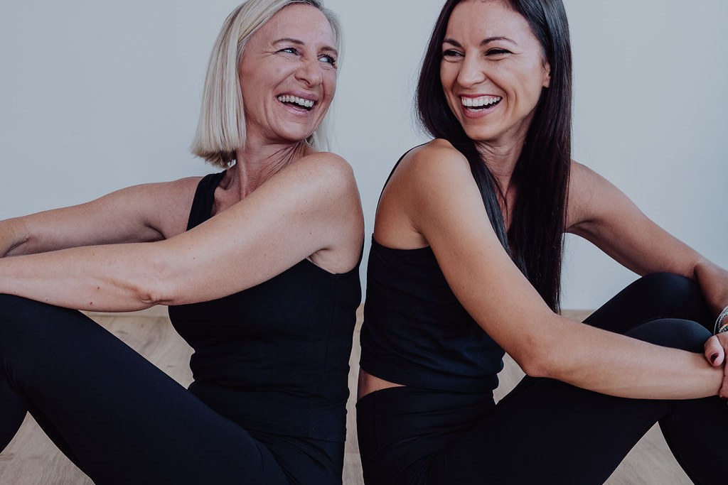 Nadine Knoll und Vanessa Kronberger sitzen lachend Rücken an Rücken auf dem Studioboden